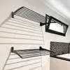 A black metal wall-mounted drying rack is shown on a white wall, with a window and a patterned backsplash visible in the background. Produktbild-Vorschau