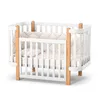 A white and natural wood baby crib is shown against a white background. Produktbild-Vorschau