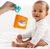 A baby is looking at a soft toy book held by an adult's hand. Anteprima dell’immagine prodotto