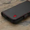 A close-up shot of a black leather phone case with red stitching and a red bull logo, resting on a textured stone surface. Anteprima dell’immagine prodotto