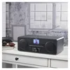 A black HAMA radio is placed on a white desk in front of a window with a brick wall. Produktbild-Vorschau