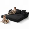A woman reads a book on a black sofa while a child and a dog play nearby. Produktbild-Vorschau