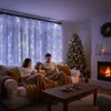 A family is sitting on a couch under a string of Christmas lights, with a Christmas tree and fireplace in the background. Podgląd zdjęcia produktu