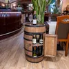 A wooden wine barrel cabinet with several wine bottles inside and two wine glasses and a bottle on top, placed in what appears to be a restaurant or bar setting. Náhled obrázku produktu