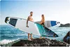 A couple holding paddleboards on a rocky shore with the ocean and sky in the background. Náhled obrázku produktu