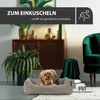 A small dog is resting in a dog bed in a cozy living room setting. Produktbild-Vorschau