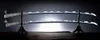 Two swords are displayed on a stand against a dark background with a bright light source behind them. Podgląd zdjęcia produktu