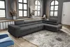 A modern living room scene with a large grey sectional sofa as the centerpiece, placed on a fluffy rug in front of large windows.