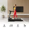A woman is exercising on a treadmill in a modern living room with a large TV on the wall. Produktbild-Vorschau