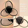 A collage of images showing a modern black LED ceiling lamp with three intertwined loops, illuminated with warm white light. Text in German describes the product. Produktbild-Vorschau