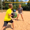 Two children are playing with boxing gloves on a sandy beach with a volleyball net in the background. Produktbild-Vorschau