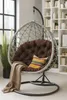 A hanging egg chair with a brown cushion and a throw blanket is shown in a room with a bookshelf in the background. Voir les images du produit