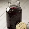 A glass jar filled with dark purple preserve, with its lid placed next to it, on a wooden surface. Podgląd zdjęcia produktu