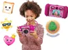 A young girl is holding a pink VTech Kidizoom Duo Pro camera, with various cartoon emojis and a dinosaur animation displayed around her. The camera is shown in use, with a screen displaying a cartoon character. Produktbild-Vorschau