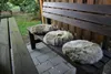 Three round, furry seat cushions are placed on a wooden park bench outdoors. Produktbild-Vorschau