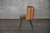 A side view of a chair with a multi-colored velvet back and black legs, set against a concrete wall and wooden floor. Produktbild-Vorschau