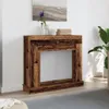 A wooden fireplace surround with a mirror inside, placed against a white wall with a painting above it. Podgląd zdjęcia produktu