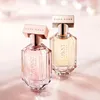 Two bottles of Hugo Boss The Scent For Her perfume are displayed on a soft pink surface with a blurred, bokeh background. Produktbild-Vorschau