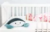 A plush crab toy sits on the edge of a white crib, with a baby lying in the crib in the background. Náhled obrázku produktu