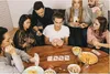 A group of friends playing cards around a wooden table, with snacks and drinks. Produktbild-Vorschau