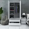 A white wardrobe and a matching chest of drawers are shown in a room with a concrete wall and tiled floor. A beanbag chair and a plant are also visible. Produktbild-Vorschau