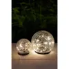 Two glass sphere solar lights with a crackle effect and internal LEDs are displayed on a wooden surface at night. Anteprima dell’immagine prodotto