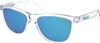 A pair of clear-framed Oakley Frogskins sunglasses with blue mirrored lenses, shown from a three-quarter angle against a white background. Náhled obrázku produktu