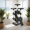 A multi-level cat tree with scratching posts and platforms is set up in a room with large windows overlooking a beach scene. Two cats are visible on the cat tree, and two potted plants are placed near the windows. Náhled obrázku produktu