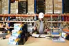 A man in a warehouse is working at a table with boxes of toner cartridges. Produktbild-Vorschau