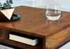 A close-up view of a wooden coffee table with a glass of water and a decorative item on it. Produktbild-Vorschau
