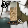 A bird feeder filled with seed in a snowy environment, with a chickadee perched on the edge. Produktbild-Vorschau