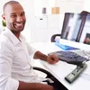 A man is sitting at a desk in an office environment, smiling at the camera. A stapler is visible on the desk. Náhľad obrázku produktu