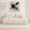 A cream-colored bouclé sofa with two large rectangular pillows and one round pillow, displayed in a minimalist room with a framed abstract painting on the wall and a potted plant. Podgląd zdjęcia produktu