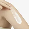 A hand is applying lotion to a leg. Voir les images du produit