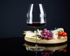 A wine glass filled with red wine sits in front of a cheese board with grapes and tomatoes. Produktbild-Vorschau
