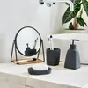 A bathroom countertop with various accessories, including a makeup mirror, soap dish, soap, toothbrush holder with brushes, and a soap dispenser. Podgląd zdjęcia produktu