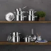 A collection of stainless steel pots and pans are neatly arranged on two wooden shelves against a dark gray wall. Podgląd zdjęcia produktu