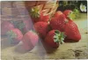 Strawberries are arranged on a wooden surface, with a basket in the background. Podgląd zdjęcia produktu