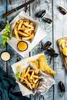 Two servings of fish and chips with mussels and dipping sauces on a rustic blue wooden table. Anteprima dell’immagine prodotto