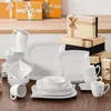 A collection of white porcelain dinnerware and gift boxes are arranged on a wooden surface. Produktbild-Vorschau