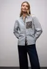 A woman is posing in a studio setting, wearing a striped shirt with leopard print accents and dark jeans. Produktbild-Vorschau