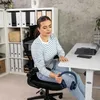 A woman is sitting at a white desk in a home office setting, holding a pair of blue headphones. Produktbild-Vorschau