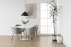 A dining room setting with a round white table and four grey upholstered chairs, a large window, a plant, and artwork on the wall. Voir les images du produit