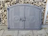 A cast iron oven door is shown in front of a stone wall and paved ground. Náhľad obrázku produktu