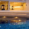 A modern building with a swimming pool and a gym visible through glass walls, illuminated by warm lights. Produktbild-Vorschau