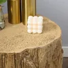 A white bubble candle sits on a textured, wood-like surface next to two gold cylindrical objects. Produktbild-Vorschau