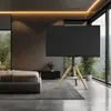 A modern bedroom with large windows overlooking a forest, featuring a TV on a tripod stand. Produktbild-Vorschau