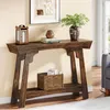 A dark wood console table with decorative elements and books on top, placed in a room with a painting on the wall and a sofa visible. Podgląd zdjęcia produktu