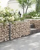 A gabion wall with stones and plants in a garden setting. Produktbild-Vorschau