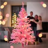 A family is gathered around a pink Christmas tree, with another decorated tree in the background. Produktbild-Vorschau